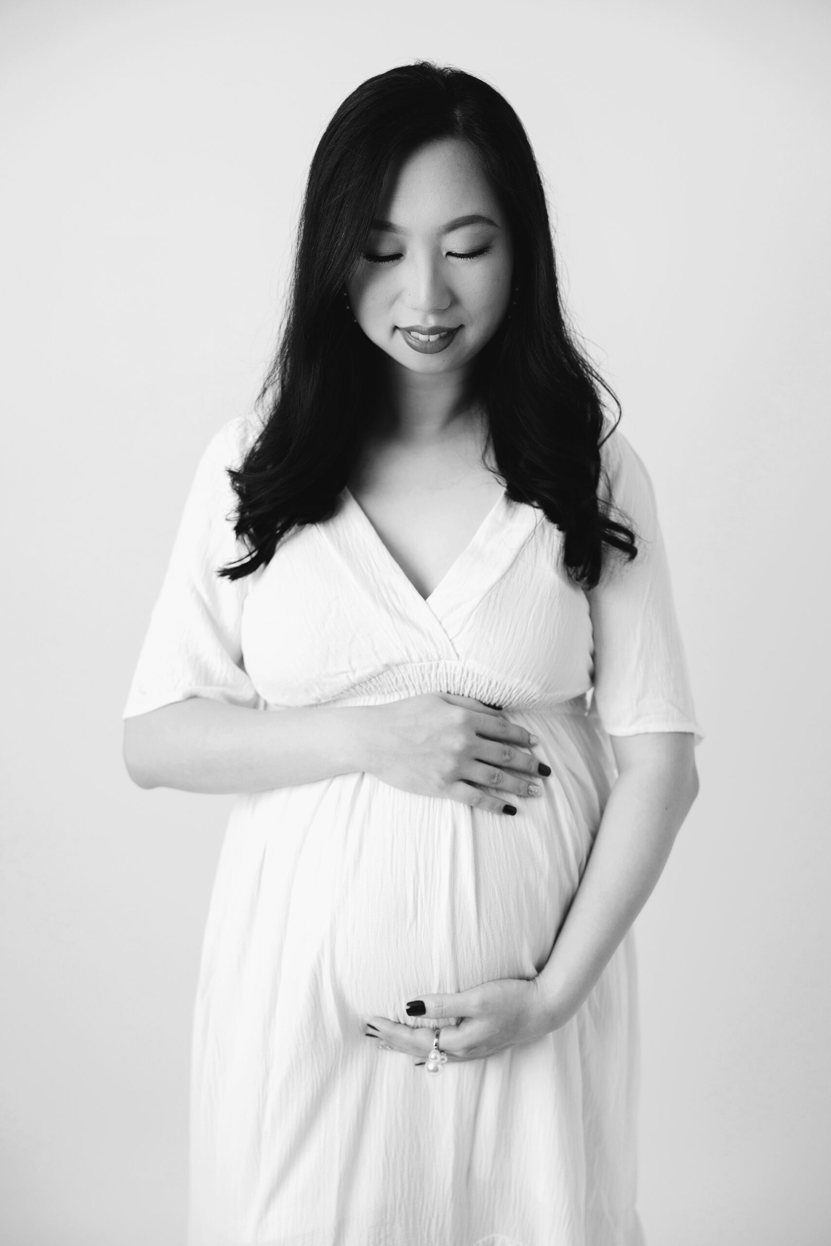 pregnant woman cradling belly and looking down in black and white- studio maternity pictures Raleigh- Laura Karoline Photography