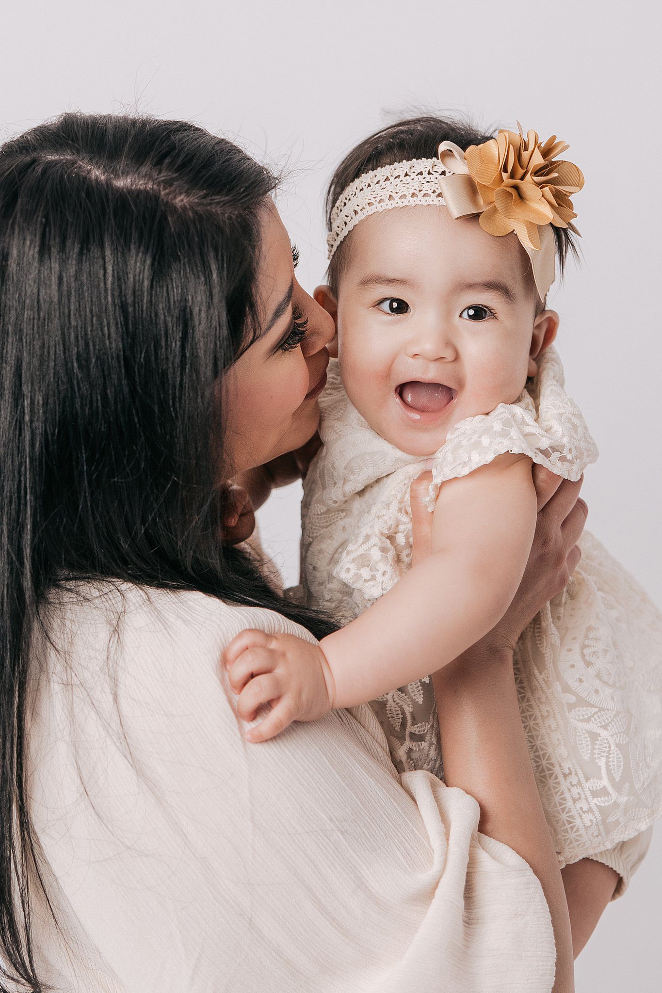 A happy mom lifts her infant daughter in a lace dress for a kiss after meeting nannies raleigh